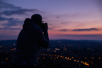 Photographer taking photos of colorful sunset on Bila Hora with amazing view on city Brno Czech...