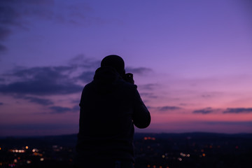 Photographer taking photos of colorful sunset on Bila Hora with amazing view on city Brno Czech Republic pink and orange colors with many clouds and city lights