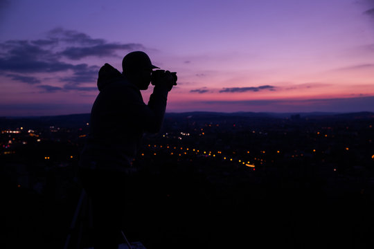 Photographer taking photos of colorful sunset on Bila Hora with amazing view on city Brno Czech Republic pink and orange colors with many clouds and city lights