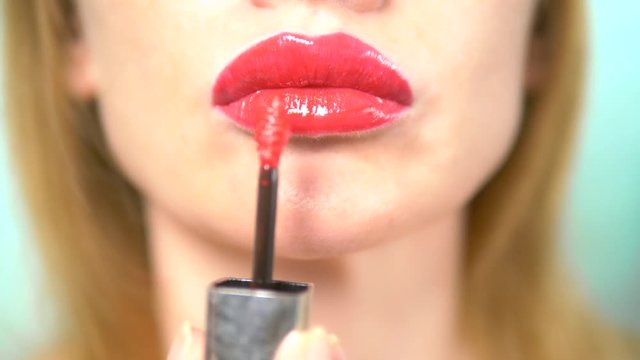 close-up. woman with beautiful sexy lips doing lip makeup with red lip gloss