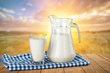 A glass of milk and a milk jug on plaid tablecloth