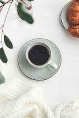 Cup of black coffee with croissant on white  table. The concept of breakfast, flat lay, top view.