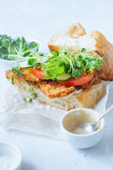 Sanwich with fried chicken on chiabatta with tomatoes, cheddar cheese, cucumber, onion, salad and microgreens