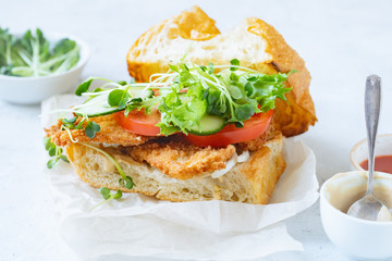 Sanwich with fried chicken on chiabatta with tomatoes, cheddar cheese, cucumber, onion, salad and microgreens