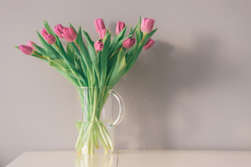 Glass vase with bouquet of beautiful tulips on grey wall background.