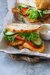 Sanwich with fried chicken on chiabatta with tomatoes, cheddar cheese, cucumber, onion, salad and microgreens