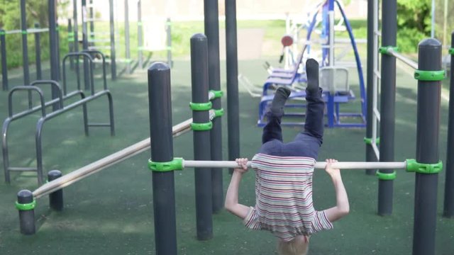 boy makes a flip ahead on the simulator. The child goes in for sports on outdoor exercise machines in the summer in the park