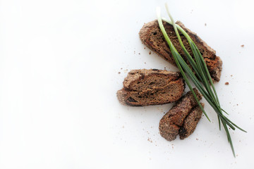 Pieces of homemade rye bread with cranberries and green onion feathers on a white background with free space for text.