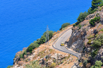 Yellow taxi car drives along the mediterranean road between mountains near the coastline