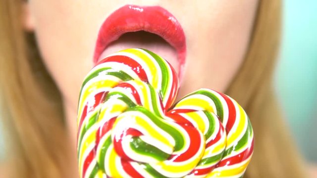 close-up, female lips with red lipstick, eat and lick a big lollipop in the shape of a heart.