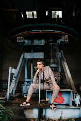 Beautiful young stylish girl posing at abandoned factory outdoor with an old broken engine.