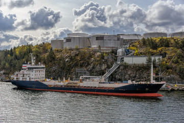 Oil/Chemical tanker sit berthed at a shore terminal with a oil product storage tanks above on...