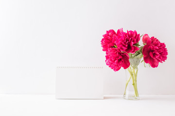Mockup white desk calendar and red peonies in a vase on a white table