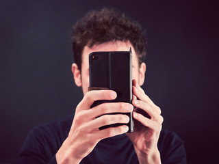 man with smartphone in front of face, front view of young person holding a mobile phone in hands (the Telephone covering his expression)
