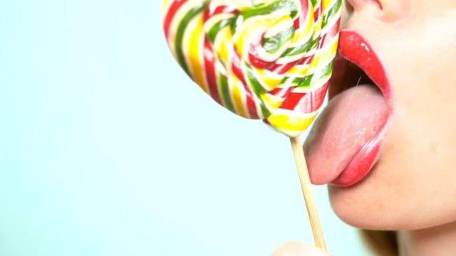 close-up, female lips with red lipstick, eat and lick a big lollipop in the shape of a heart. copy space, blue background