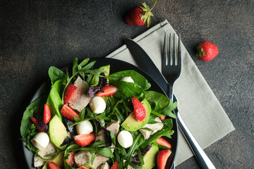 Salad with fresh strawberries, arugula, basil, avocado and mozzarella on a dark background.