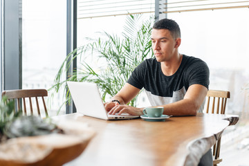 Freelancer work on netbook in modern coworking. Young man drinking coffee from a Cup. Programmer at remote job. Successful people, businessman in comfortable cafe. High large Windows