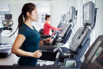 Fototapeta premium Side view of woman exercising on treadmill in gym