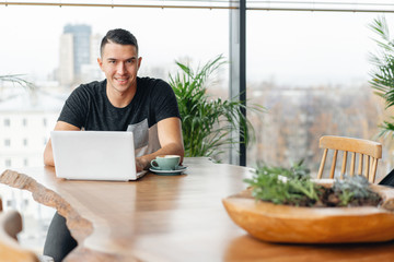 Successful people, businessman in comfortable cafe. Freelancer work on netbook in modern coworking. Young man drinking coffee from a Cup. Programmer at remote job. High large Windows