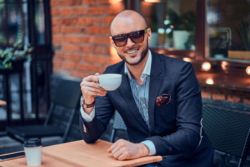 Elegant smiling man is drinking coffee while sitting outside at cafe on his break.