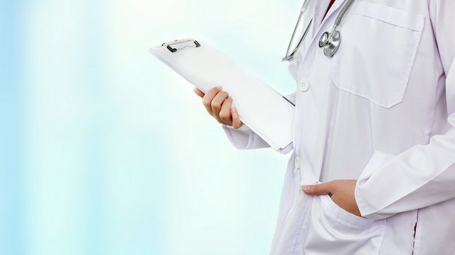 Close Up Female Doctor With Stethoscope In Thinking Gesture And Holding Clipboard With Blurred Pale Blue Medical Office Background, Medical Healthcare Concept