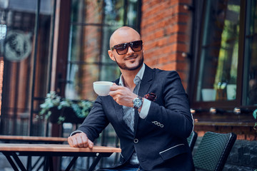 Elegant smiling man is drinking coffee while sitting outside at cafe on his break.
