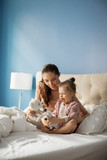 Mother and daughter playing with stuffed toys while sitting on bed at home