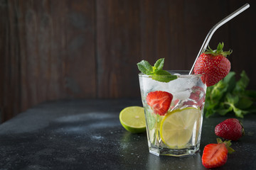 Detox lemonadeor mojito with lime, lemon, strawberry in rocks glass. Summer healthy freshness drink. Horizontal orientation. Dark wooden background. Space for text.