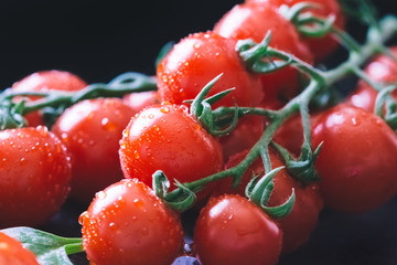 Fresh, wet cherry tomatoes on a black background with spices, macro photo