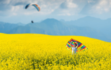 Little boy in white shirt running with kite in the booming yellow field on summer day.