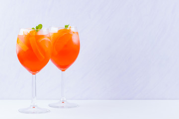 Aperol Spritz cocktail with mint leaves on a white background. A glass of summer alcohol cocktail with orange slices. Classic Italian drink coral color