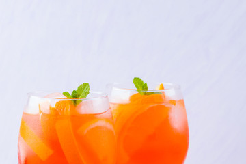 Aperol Spritz cocktail with mint leaves on a white background. A glass of summer alcohol cocktail with orange slices. Classic Italian drink coral color