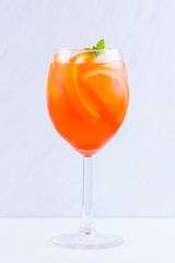 Aperol Spritz cocktail with mint leaves on a white background. A glass of summer alcohol cocktail with orange slices. Classic Italian drink coral color