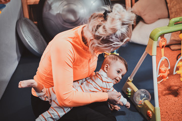 Joyful happy mom is playing with her newborn baby while waiting for a doctor at pedeatrician cabinet.