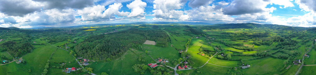 Aerial wide panoramic view on sudety mountains with touristic city in the valley surrounded by meadows, forest and rapeseed fields
