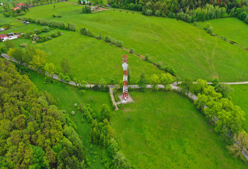 Aerial view on steel telecommunication tower in green land with meadow, forest and village