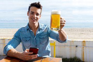 Front view of young man sitting on a beach club while using a mobile phone in a sunny day