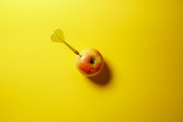 Yellow arrow dart hitting the target apple isolated on yellow background. Minimal idea food and...
