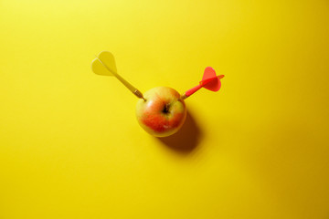Yellow arrow dart hitting the target apple isolated on yellow background. Minimal idea food and fruit concept