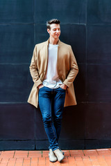 Young man wearing winter clothes walking in the street. Young with modern hairstyle in urban background
