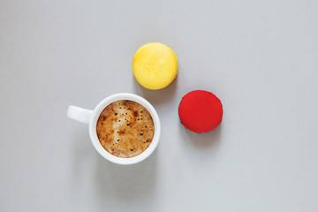 cup of coffee and pair of colorful macarons or macaroons on gray background, top view, flat lay
