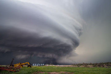 A huge supercell storm with a ground scraping wall cloud fills the sky over Nebraska farmland.
