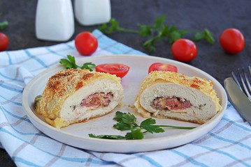 Homemade fillet Cordon Bleu or chicken fillet with ham and cheese on a white clay plate on a dark brown background. Swiss cuisine. Selective focus.
