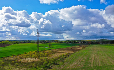 Aerial perspective view on rural landscape with house, forest, clouds, fields and electric power line tower