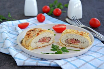 Homemade fillet Cordon Bleu or chicken fillet with ham and cheese on a white clay plate on a dark brown background. Swiss cuisine. Selective focus.