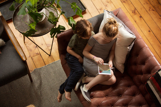 High angle view of siblings playing games over tablet computer while sitting on sofa at home