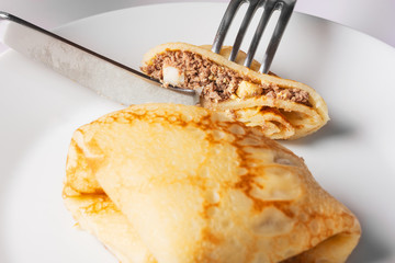 Female chef cutting pancakes with a meat, eggs and onions stuffing. White background. Close up. Selective focus.