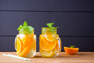 Infused water with orange, lemon and mint. Mug delicious refreshing drink of mix fruits with mint on wooden boards. Iced summer drink in mason jar. Homemade detox cocktail