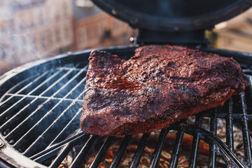 Close up on the blackened and charred bark of a smoked beef brisket, in a slow cooking background