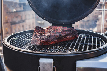 Close up on the blackened and charred bark of a smoked beef brisket, in a slow cooking background